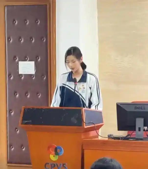 会议厅整齐的长桌、立式话筒，一身干净校服的小姑娘端坐台前低头念稿，眉眼清秀安静，