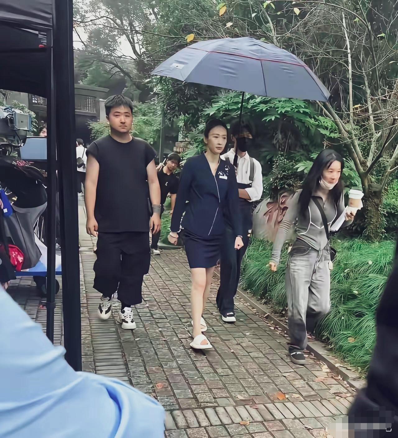 童瑶沉稳气场。一身正装，踩着拖鞋，身后工作人员随行撑伞，挺有排面的。