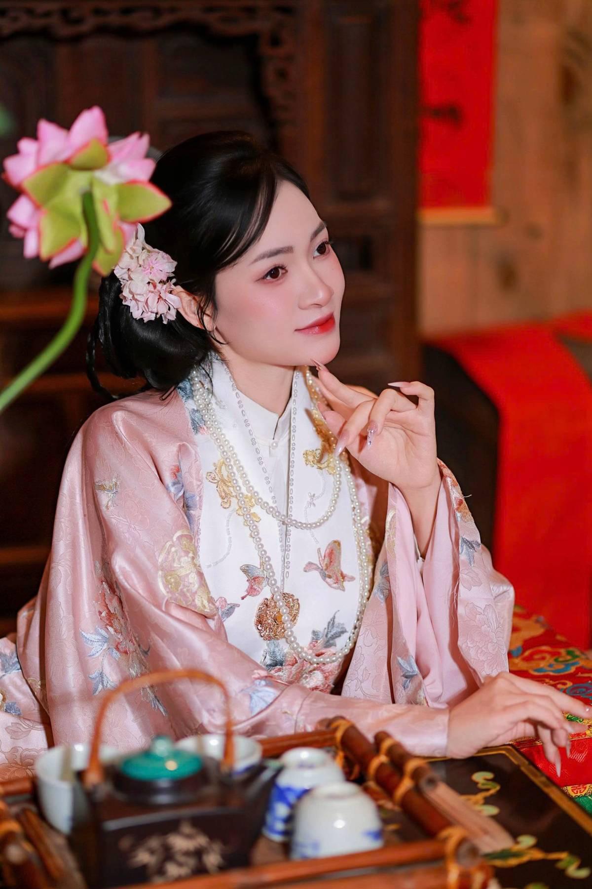 一袭粉衣绾起长发，垂眸执花倚在木廊，身旁油纸伞静立，檐下繁花轻垂。
没有浓艳的修