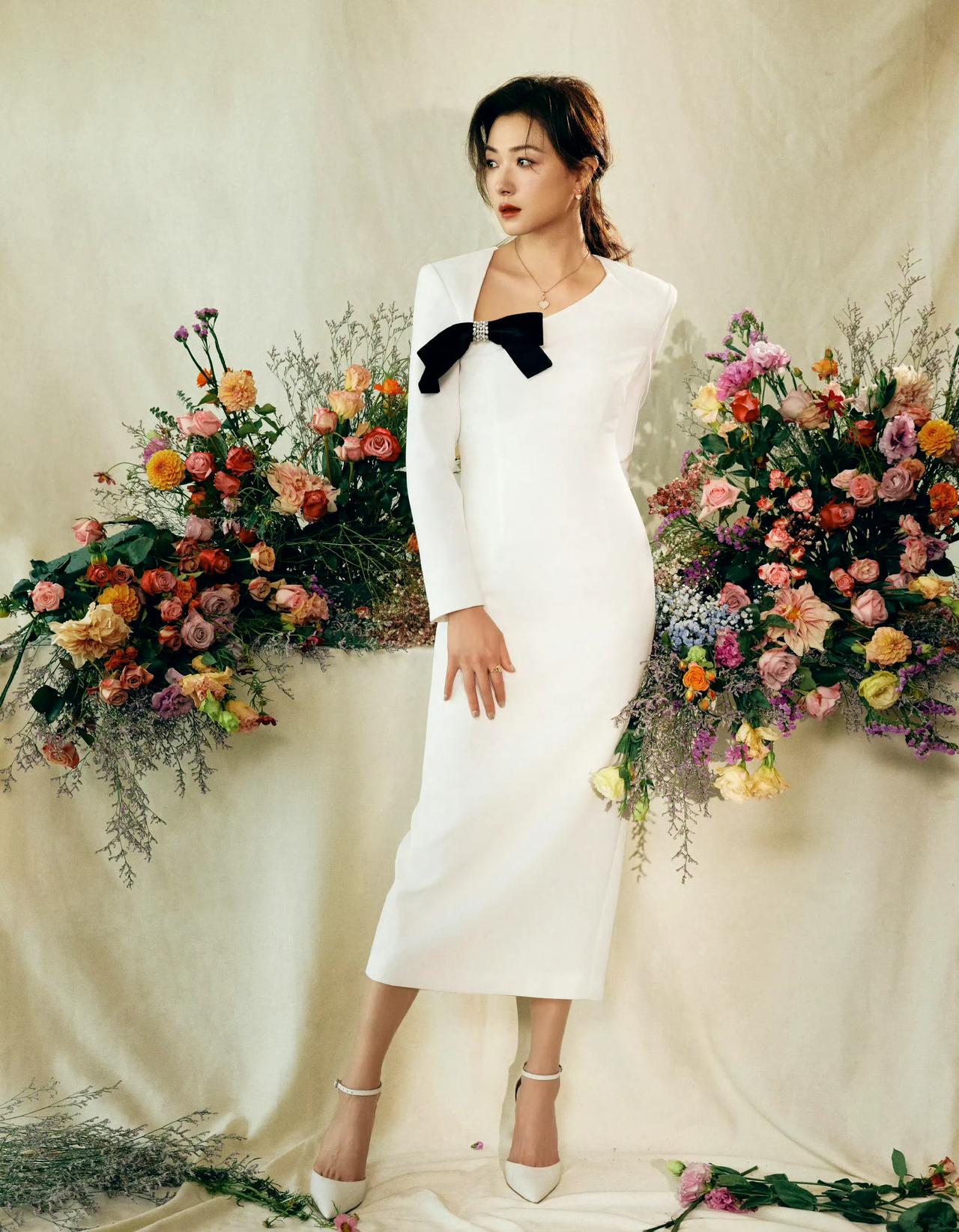 一袭白裙，略显凌乱的发型。精致的妆容！呆萌的眼神。她就和她后面的花儿一样，美的鲜