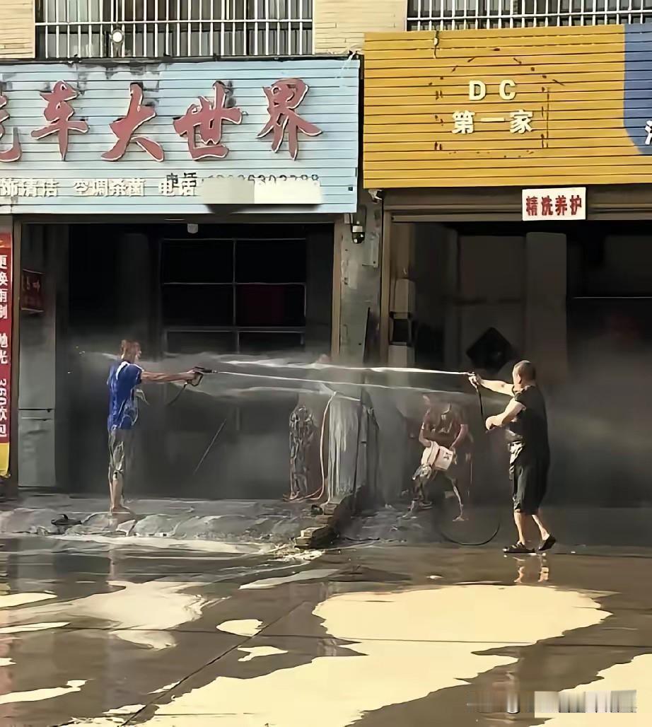 仅一墙之隔的两家洗车店，因为抢生意发生口角后，两家的男人拿着水枪对喷，女人则是拿