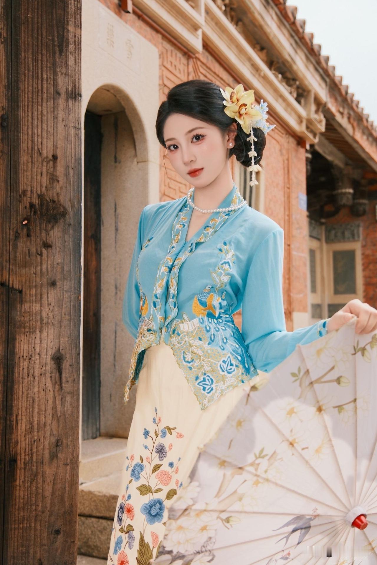 红砖燕尾脊，古韵遇南洋，清浅蓝衣缀满精巧刺绣繁花长裙步步生韵，油纸伞轻握，穿梭百