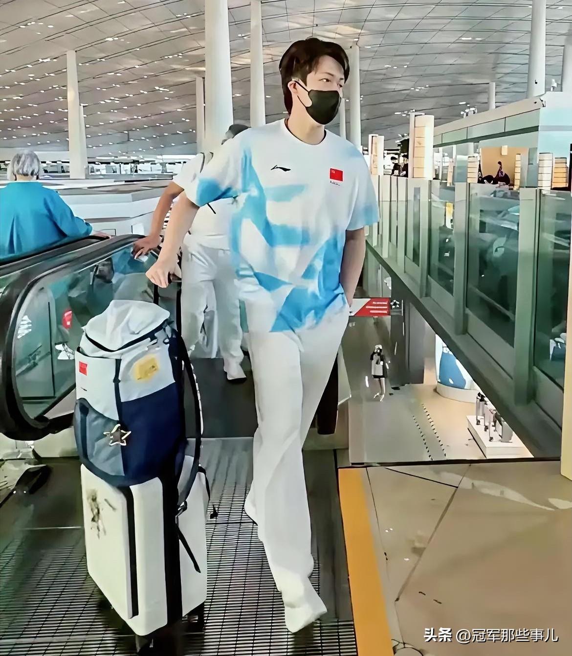 王楚钦一身蓝白出征新队服，一只手推行李箱，另一只手插裤兜，从容走在队伍前方，被球