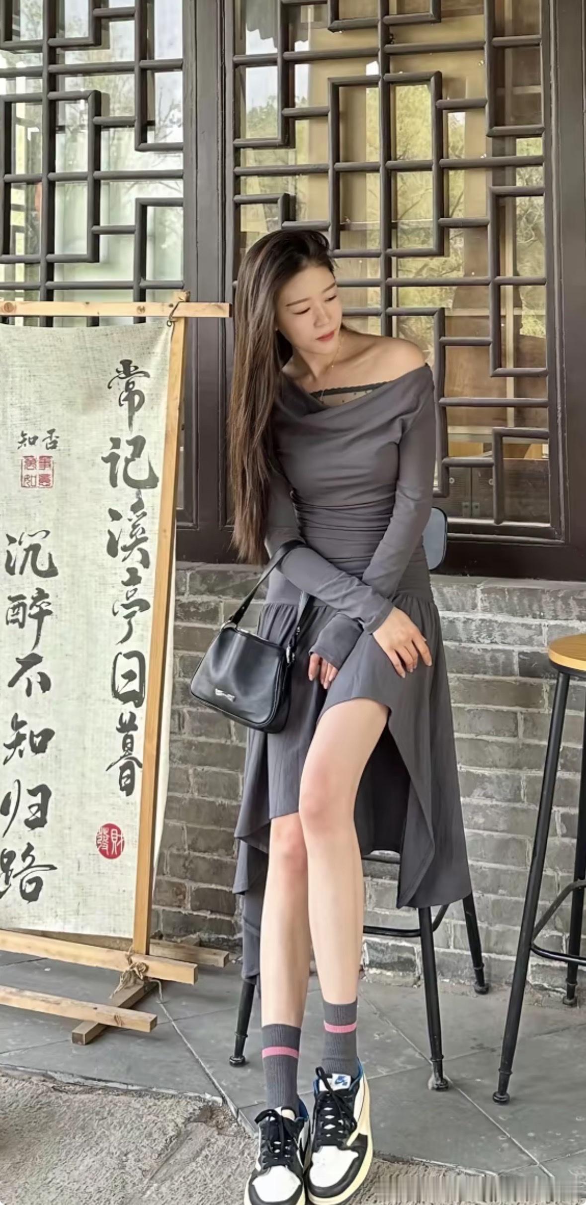 灰裙女子优雅端坐湖畔木台，单手轻拢秀发，姿态慵懒迷人。露肩设计展露优美锁骨，搭配