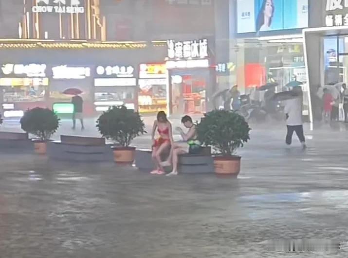 辽宁沈阳，外面下着大暴雨，不少人都躲在商场门口躲雨，但一对年轻男女却穿着泳装，拿