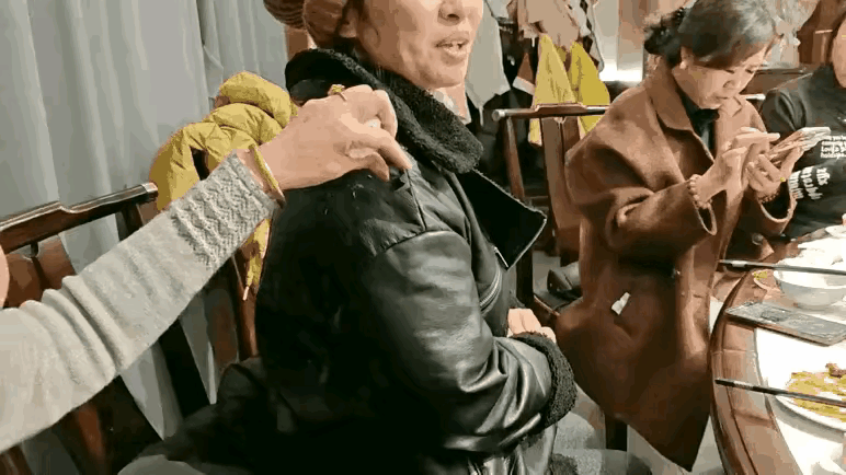 酒桌上本来挺热闹，一桌子人正聊着，突然就见个女的伸手，直接从旁边黑衣女子衣服上撕