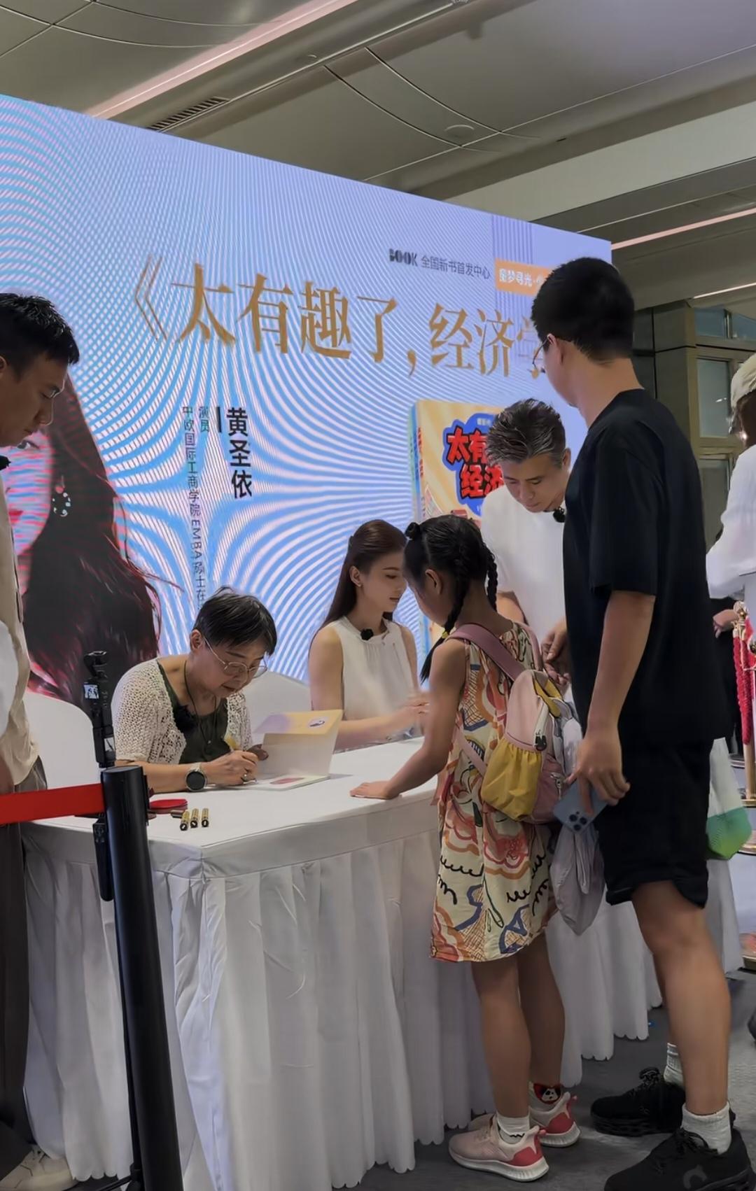 黄圣依穿白色裙子，
气质温婉，
与妈妈一起线下签售由她主编的儿童财商启蒙书《太有