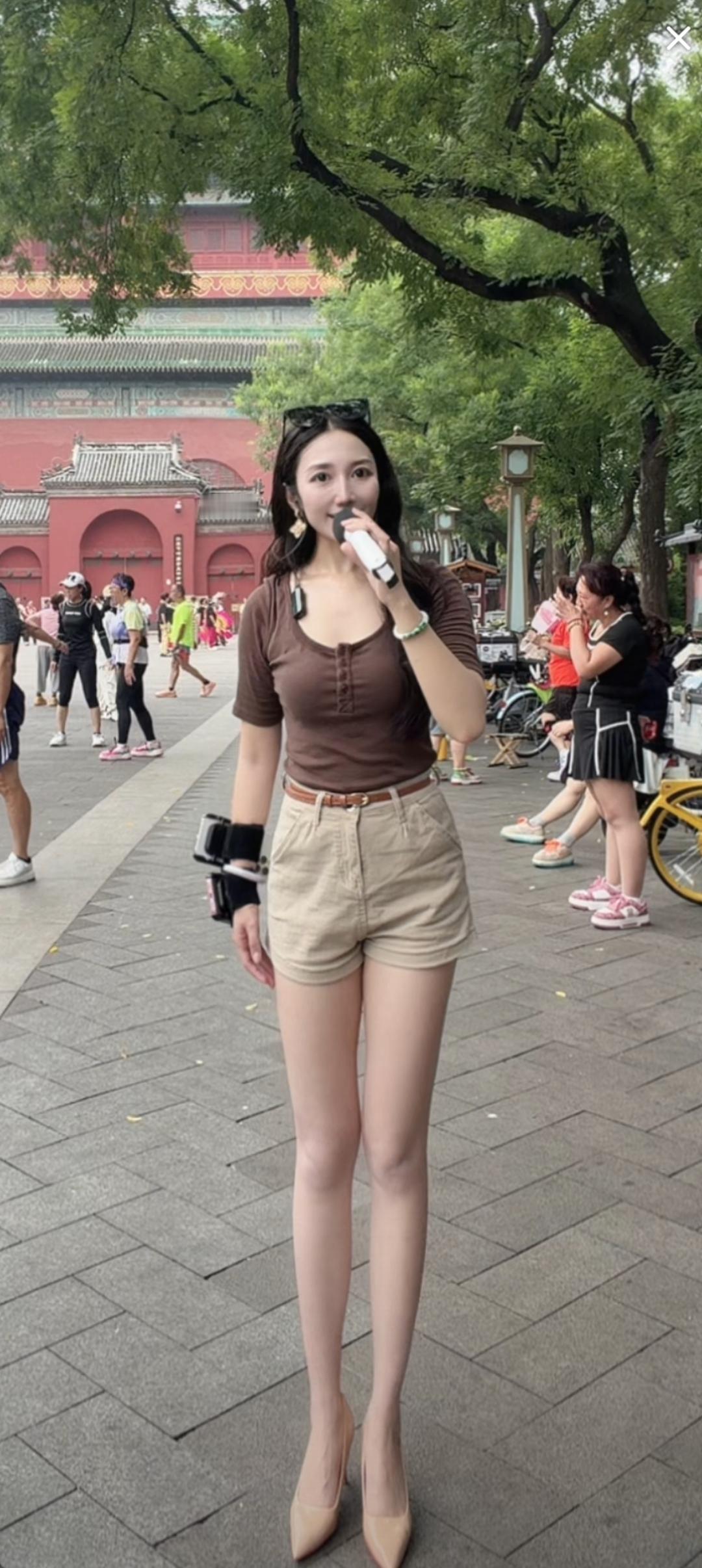 一个女孩在户外自拍，背景是红墙绿树。