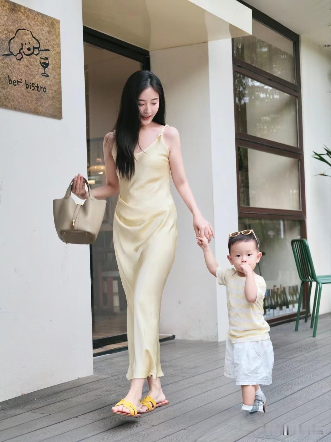 妈妈带着小孩出门散步。
时尚妈妈，穿搭贵气，手拉孩子上街，幸福感满满。