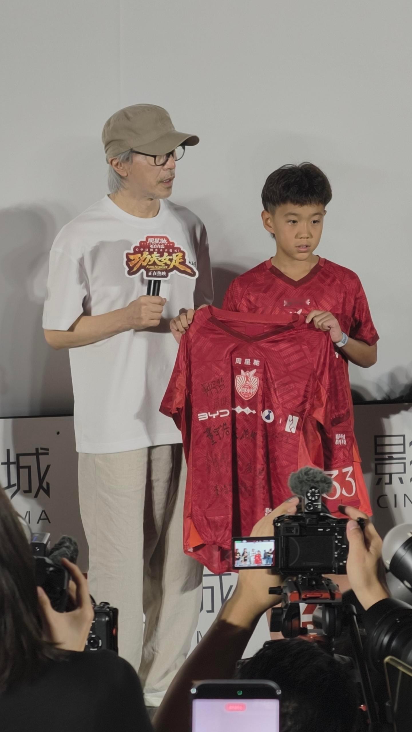 《功夫女足》路演现场，周星驰和一位穿比亚迪定制队服的足球少年定了个约：世界杯见。