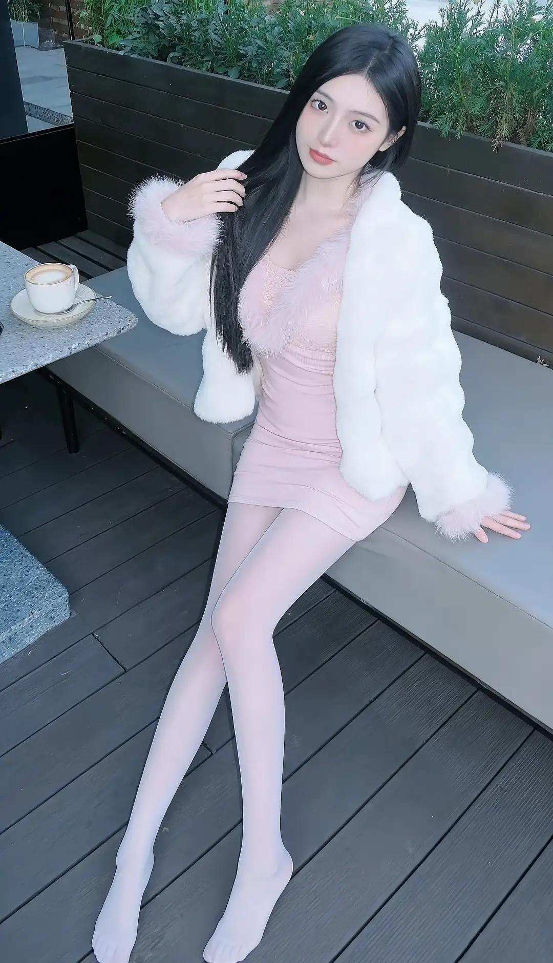 图片中的场景是一个户外休闲区域。一位女性坐在灰色的长椅上，她穿着粉色的连衣裙和白