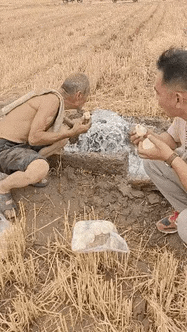 男子和一位大爷在田间地头吃着买来的包子，大爷随即喝了一口旁边的井水，男子也过去尝