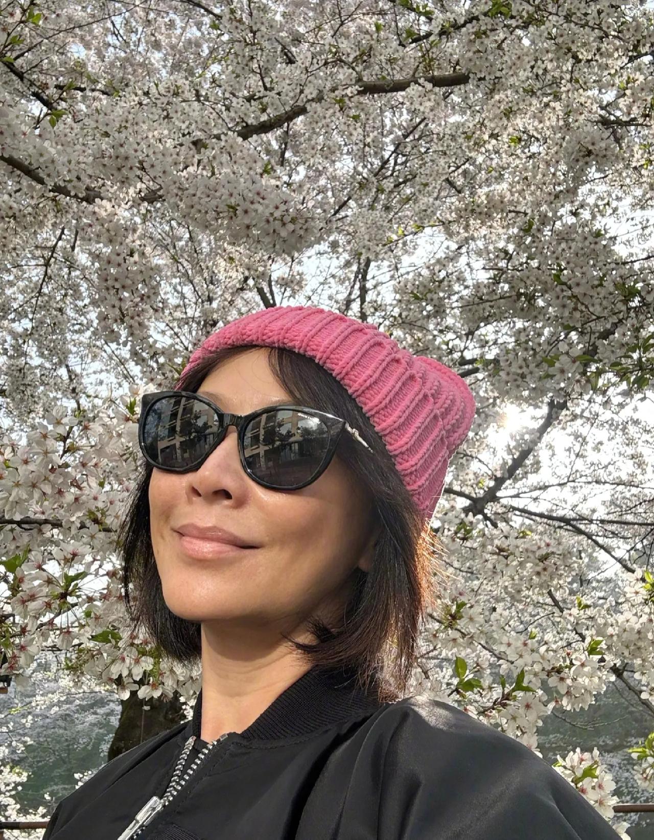 刘嘉玲在日本游玩，赏樱花，素颜状态真好，完全不像58岁的人。戴着粉色针织帽，站在
