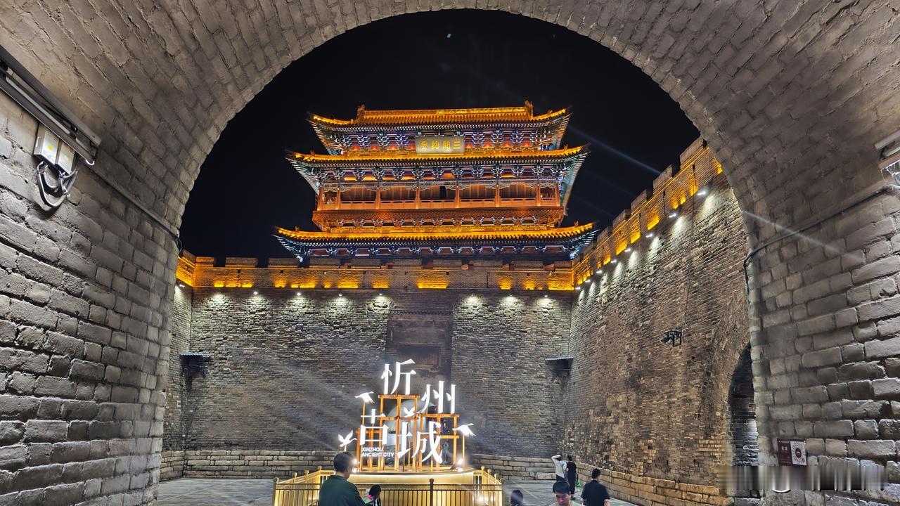 雨歇云散，夜幕轻笼忻州古城。青石板泛着水光，檐角灯笼摇着暖黄。巷口小吃飘香，古楼
