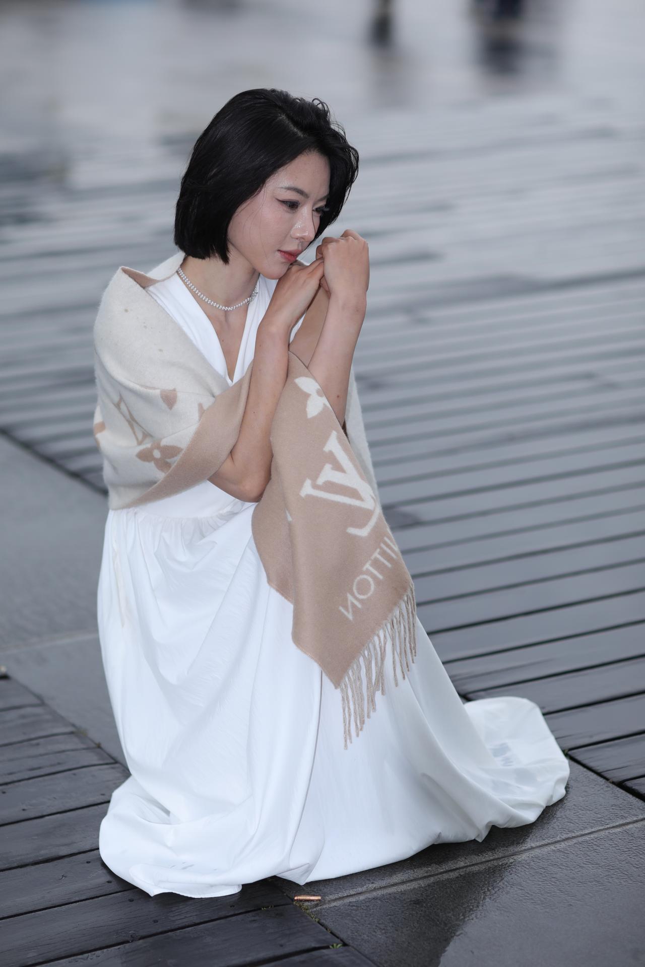 《白裙与湿岸》
雨湿的木栈道上，她身着一袭素白长裙，垂坠的面料裹着温柔的曲线，浅