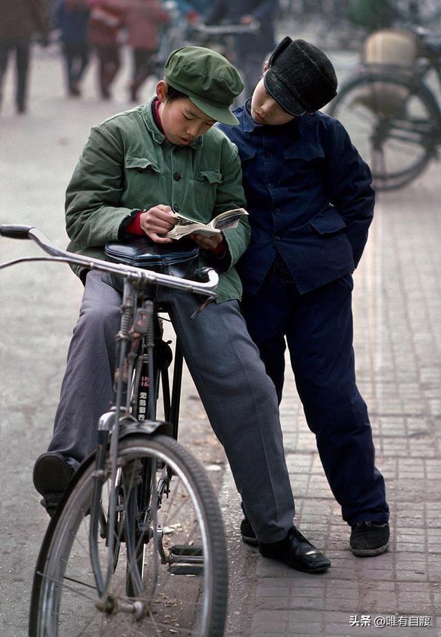 这是八十年代的孩子，一起看小人书。
其中一个孩子还骑上了自行车，戴上了绿色军帽。