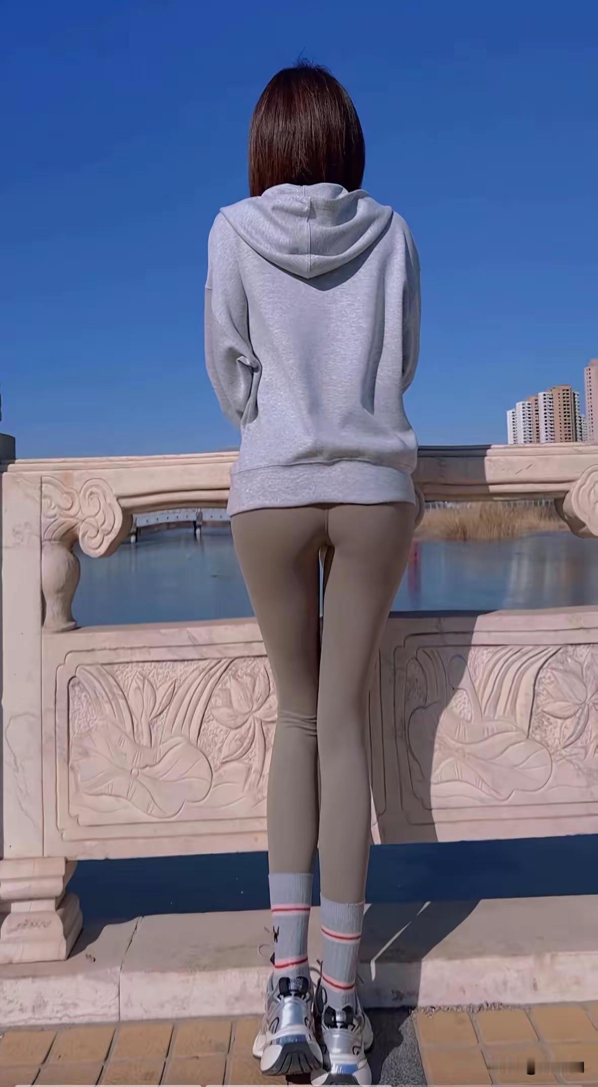 桥栏靠个俏娇娥，灰衫松垮腰婀娜！
浅裤绷出长腿细，潮鞋袜边粉杠多！
湖光蓝天衬她