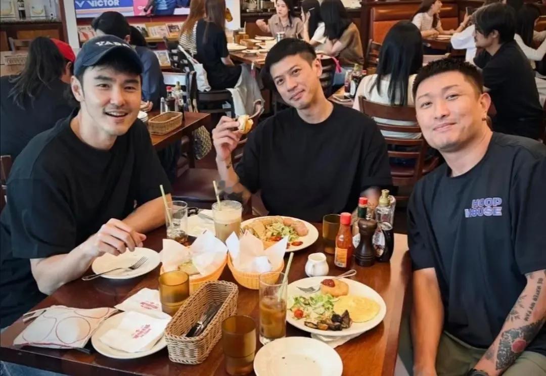 阮经天和友人聚餐，店内客流爆满，二人索性靠着墙面在门口等候，穿搭风格相近，相处随