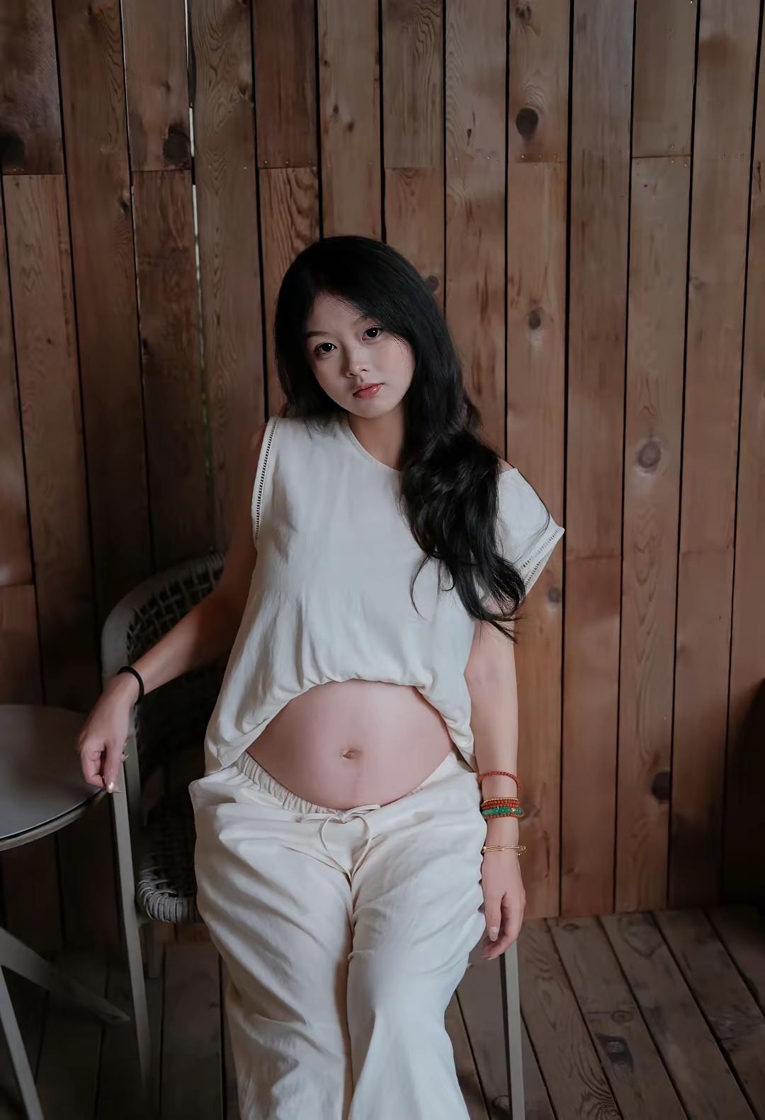 这姑娘在木墙前坐着，穿着白色衣服。