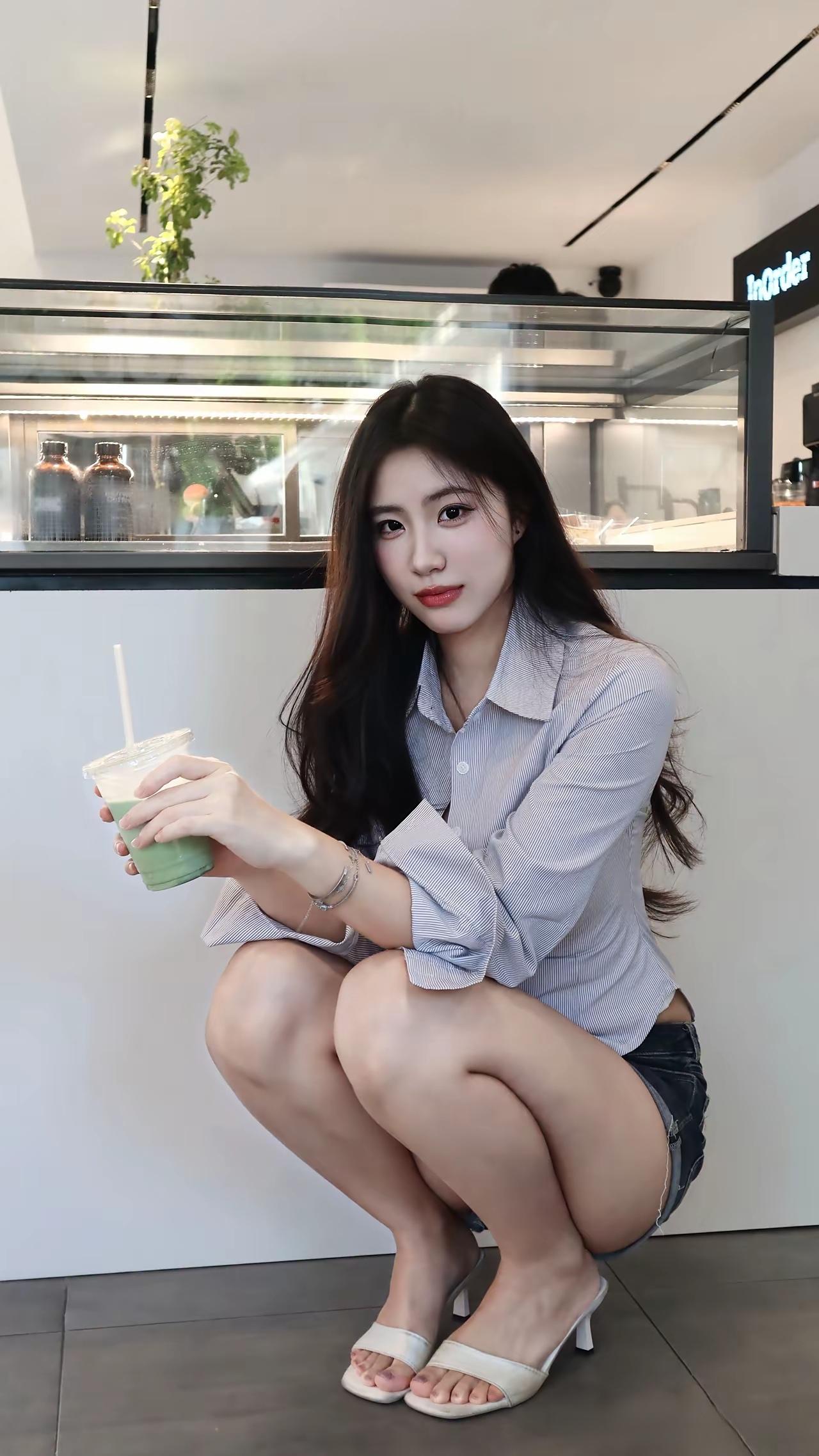 浅蓝色条纹衬衫搭配牛仔短裤，随性且不失精致感。手捧抹茶饮品，于光影交错之中，将咖