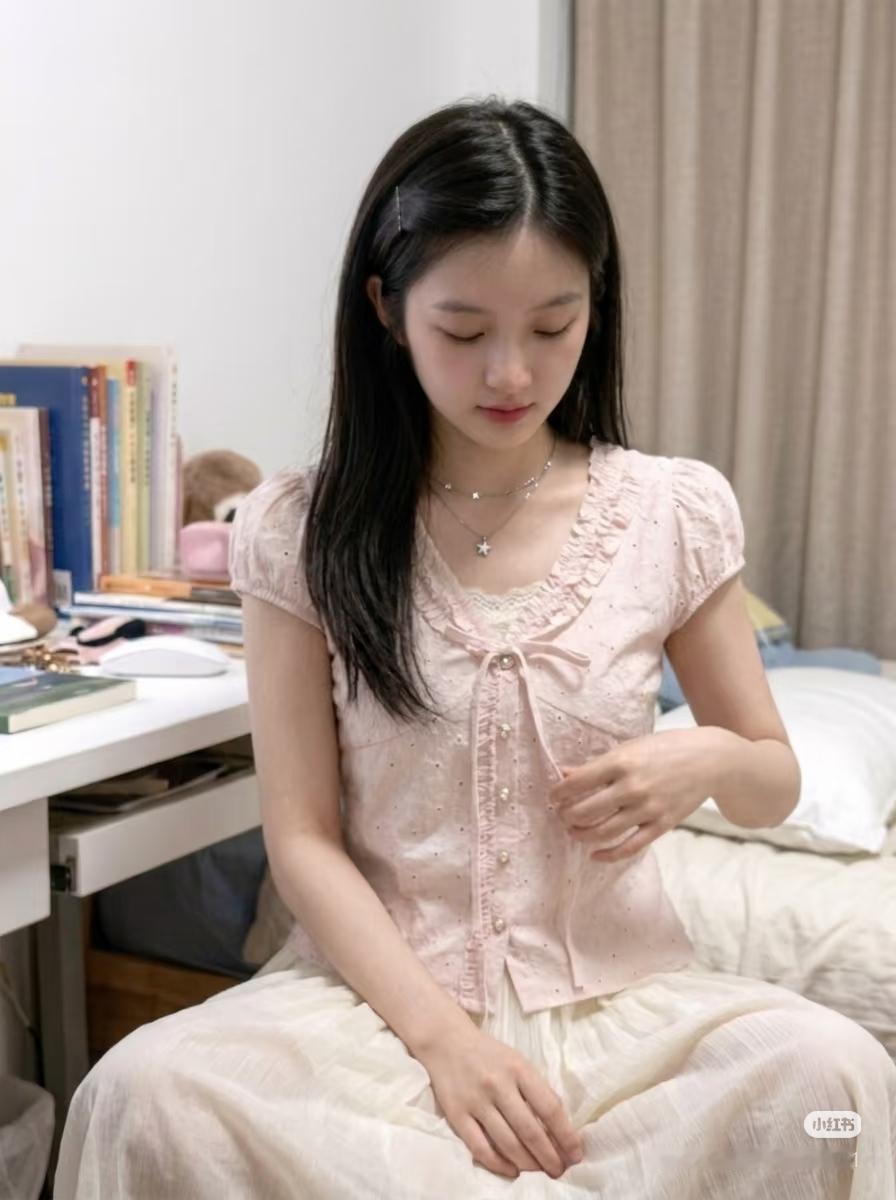邻家甜妹穿着粉色连衣裙坐在书桌前，看着手机。