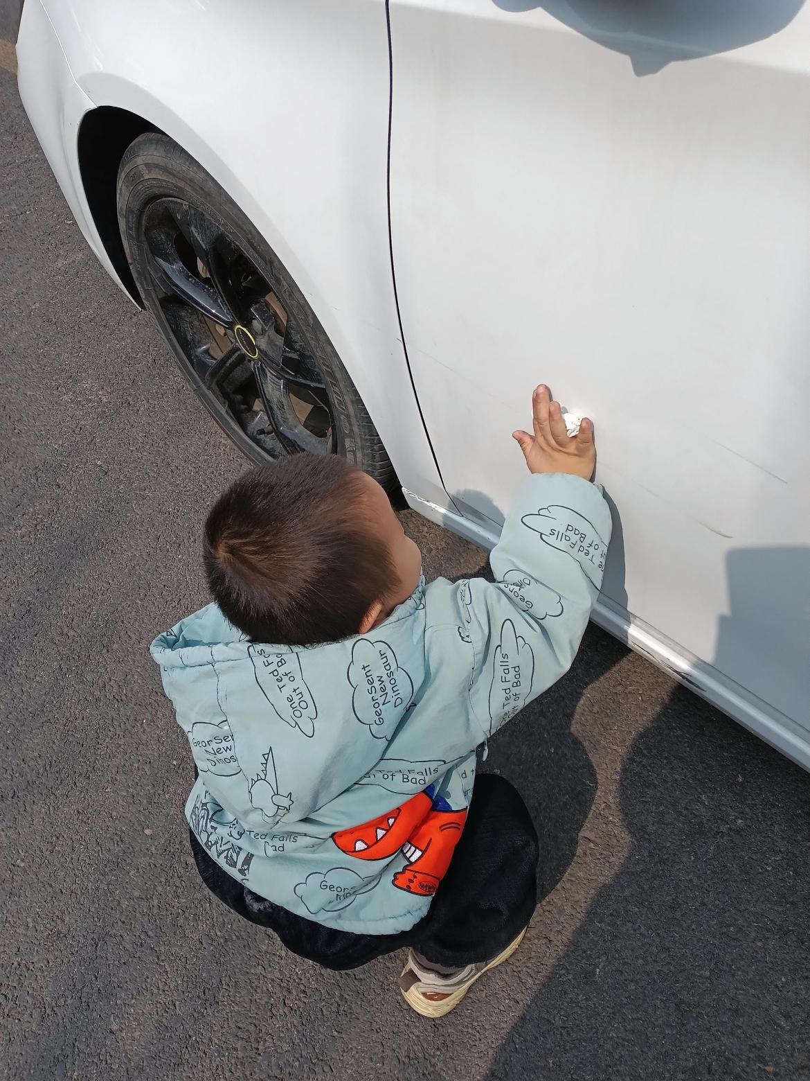 小宝宝踮着脚尖，拿着小抹布认真给爸爸擦汽车，小短腿挪来挪去，抹布在车身上胡乱比划