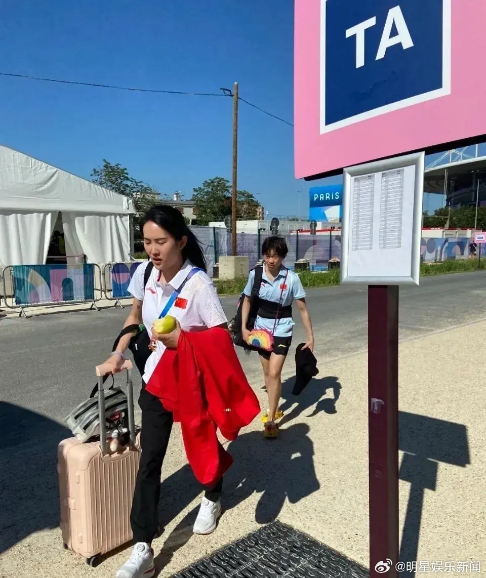 陈若琳和全红婵前往奥运村，陈若琳左手拿着梨右手拉着行李箱，全红婵背了一身娃娃，师