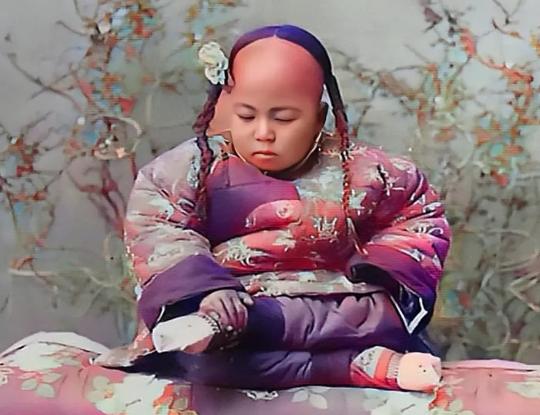 1900年，地主家的小千金，她身穿一件华丽的棉袄棉裤，衣料是当时最为贵重的丝绸，