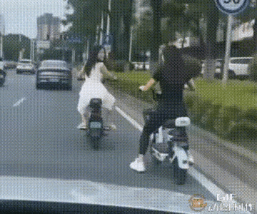 两个女孩儿在车来车往公路上追逐嬉闹，这也太危险了！现在摔到绿化带里算是最好的结局