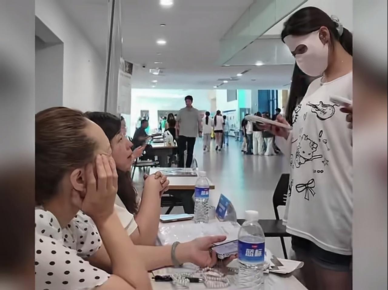 在人才招聘市场，和人说话，除了戴着面罩，还手里拿着手机平放，大拇指在上方，准备着