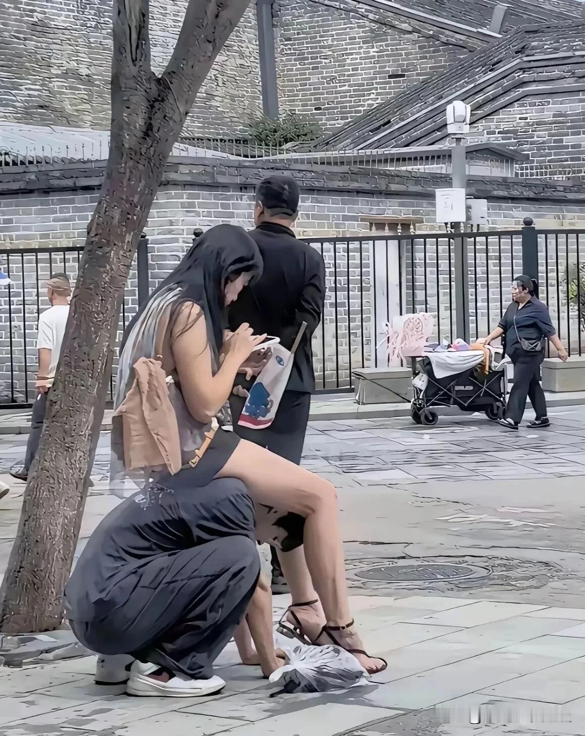 这样做就是真的爱情吗？大街上男孩和女友一起出来玩，没有凳子，男孩子蹲在地上让女友