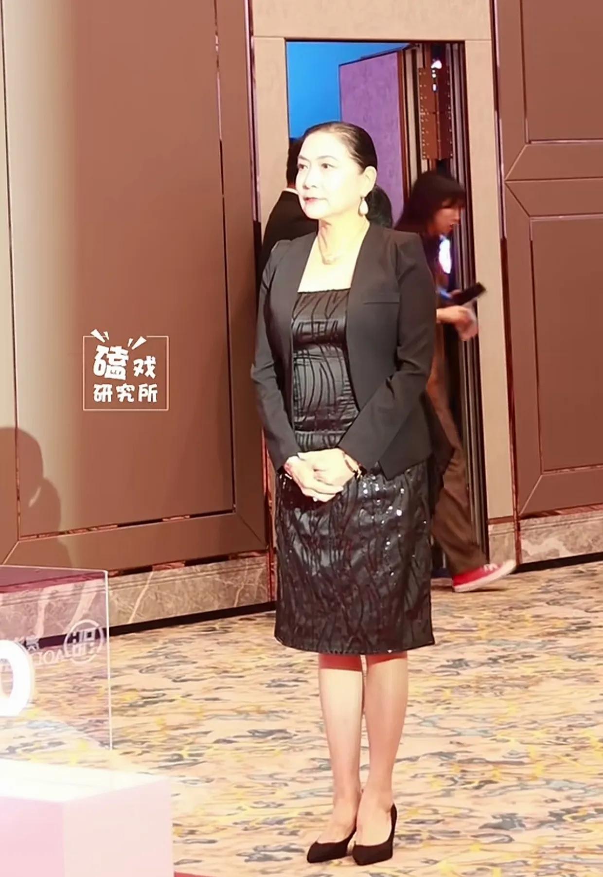 一条黑色的连衣裙外搭一件黑色的小外套，头发向后扎成了一个马尾。64岁的沈丹萍又一