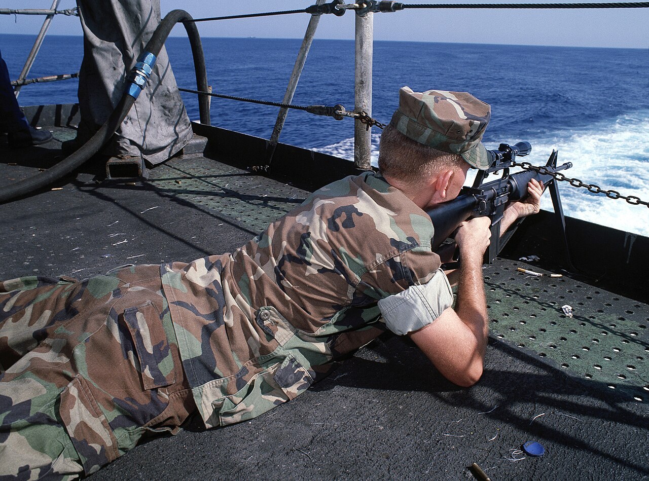 1987年，一名美国海军陆战队员正在军舰甲板上使用带瞄准镜的M16A1步枪进行射
