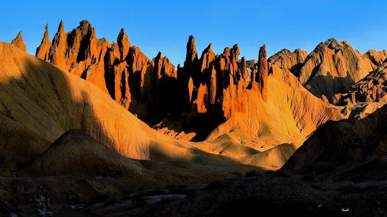 阳光洒落峡谷，红褐色的土峰林立如戟，光影在沟壑间起伏流转。孤岩静立山巅，群峰刺破