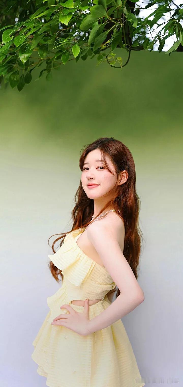 阳光明媚的午后，一位穿黄色连衣裙的少女在绿意盎然的背景下微笑，那画面简直美极了。