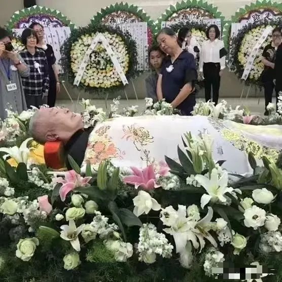 这是陈小鲁的告别仪式现场，他是陈毅元帅幼子。他安详躺卧于鲜花丛中，身着素衣，盖着
