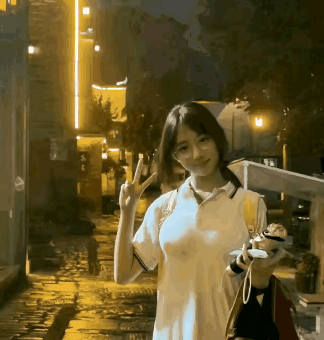 夜晚的街头，少女手持小玩偶，微笑比出V字手势，温暖灯光下的美好瞬间。
