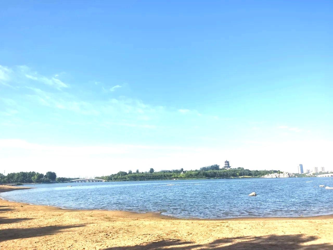 可以分享一张最美湖面的照片吗夏日清晨的清风湖，阳光洒在沙滩上，蓝天白云下的湖心岛