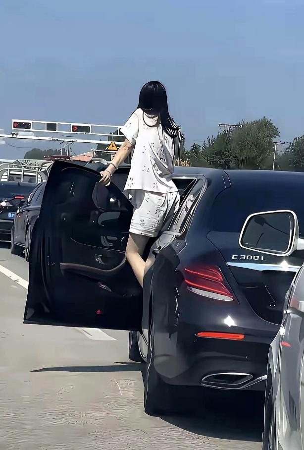 国庆出去旅游，在高速路上大堵车，一名穿着睡衣的年轻女司机打开车门眺望前方，看到前