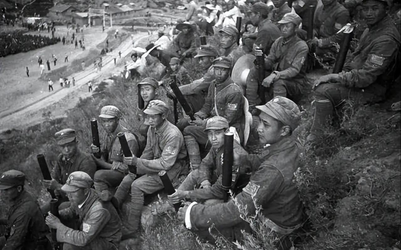 照片里的八路军战士们身着灰布军装、头戴制式军帽，臂佩八路军臂章，整齐坐在山坡高地