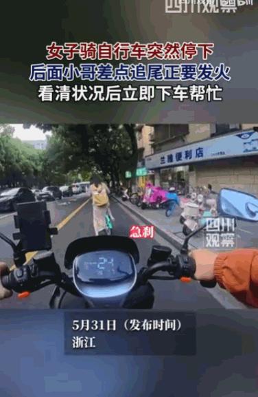 "出门在外，互帮互助。"一位女士骑着自行车突然在路中间停下，后方一位骑着电动车的