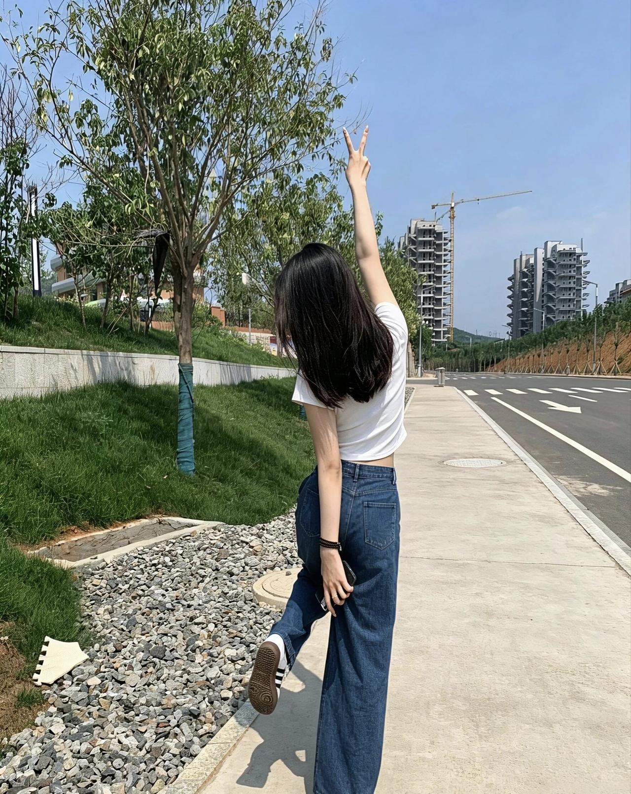 阳光明媚的一天，少女在街头摆出俏皮姿势，背景是绿树和现代建筑。