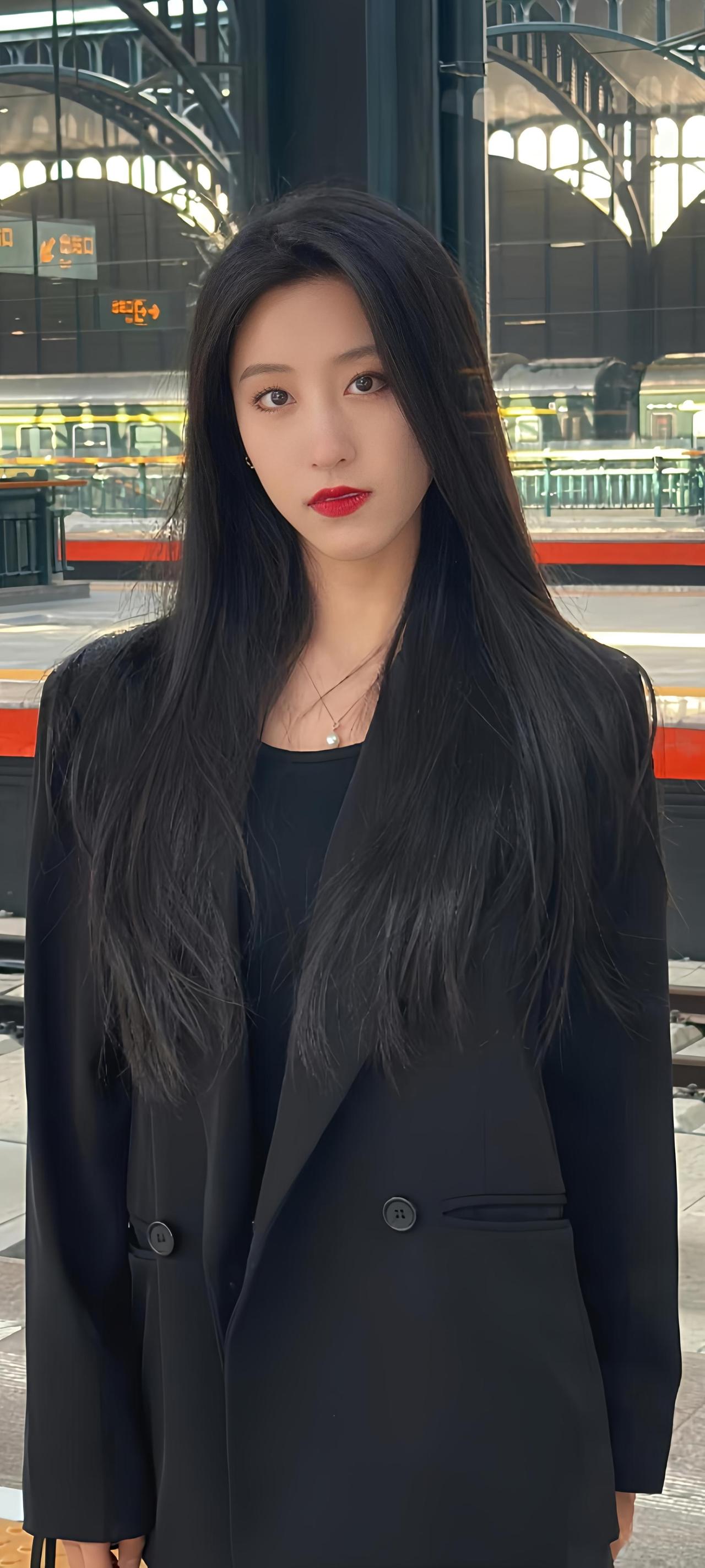 一个穿黑色西装外套的美女站在车站。