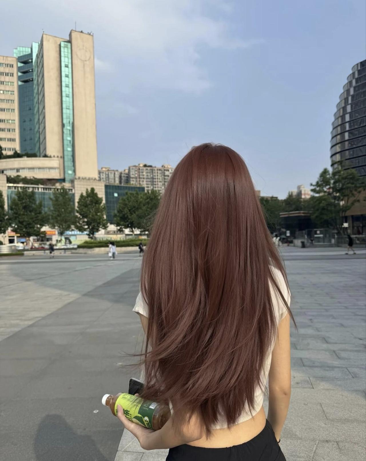 阳光下的长发少女，漫步在城市广场，手拿饮料，享受悠闲时光。