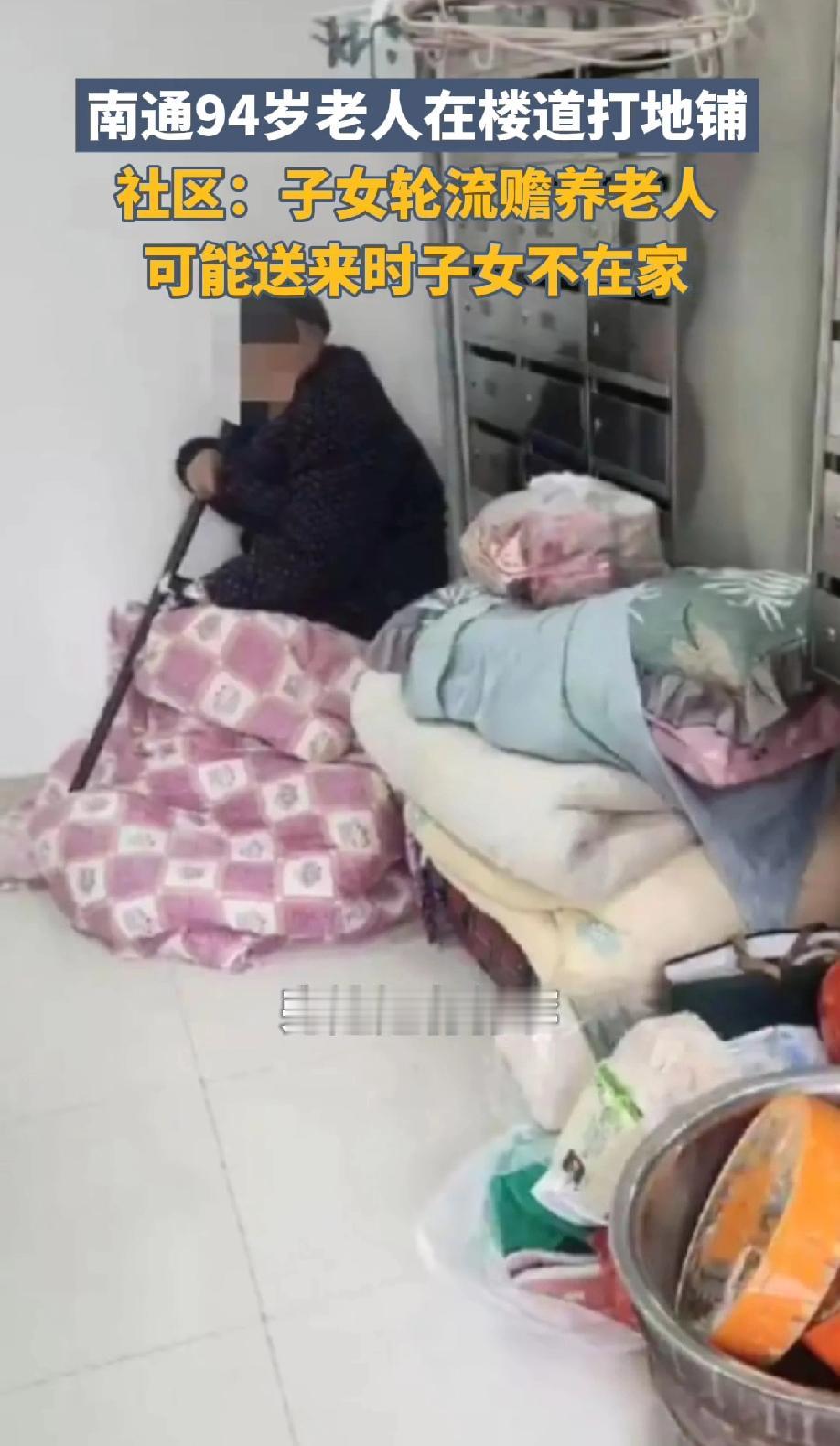 江苏南通，一个小区的楼道里，一位94岁的老人居然独自一人裹着一床粉白格子的旧棉被