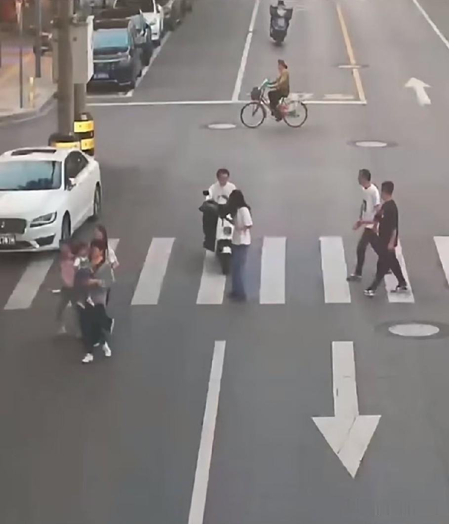 山东菏泽，在一个没有红绿灯的路口，行人女子过斑马线看着手机，男子单手骑电动车也看