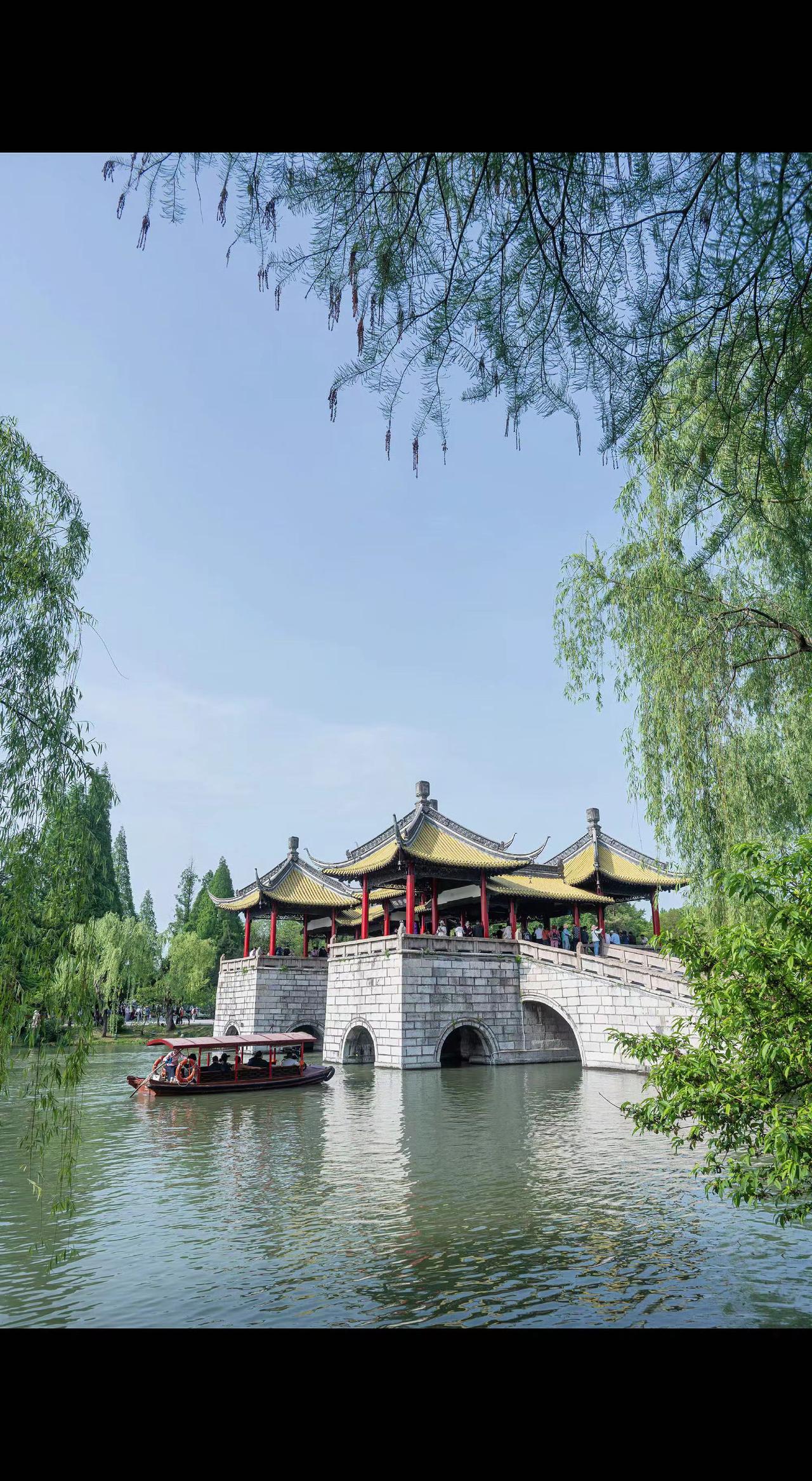 🌿柳丝垂成帘，画舫裁开水面📖。飞檐驮着云，桥洞偷藏天光✨。此刻岁月是幅慢卷轴