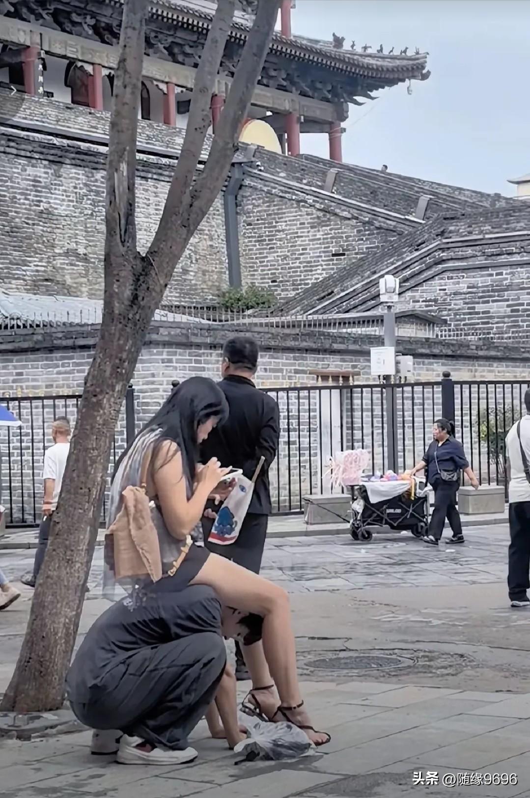 一位年轻女子露胳膊露腿，悠然自得地骑在男子的脖子上专心致志地玩手机，而被骑的男子