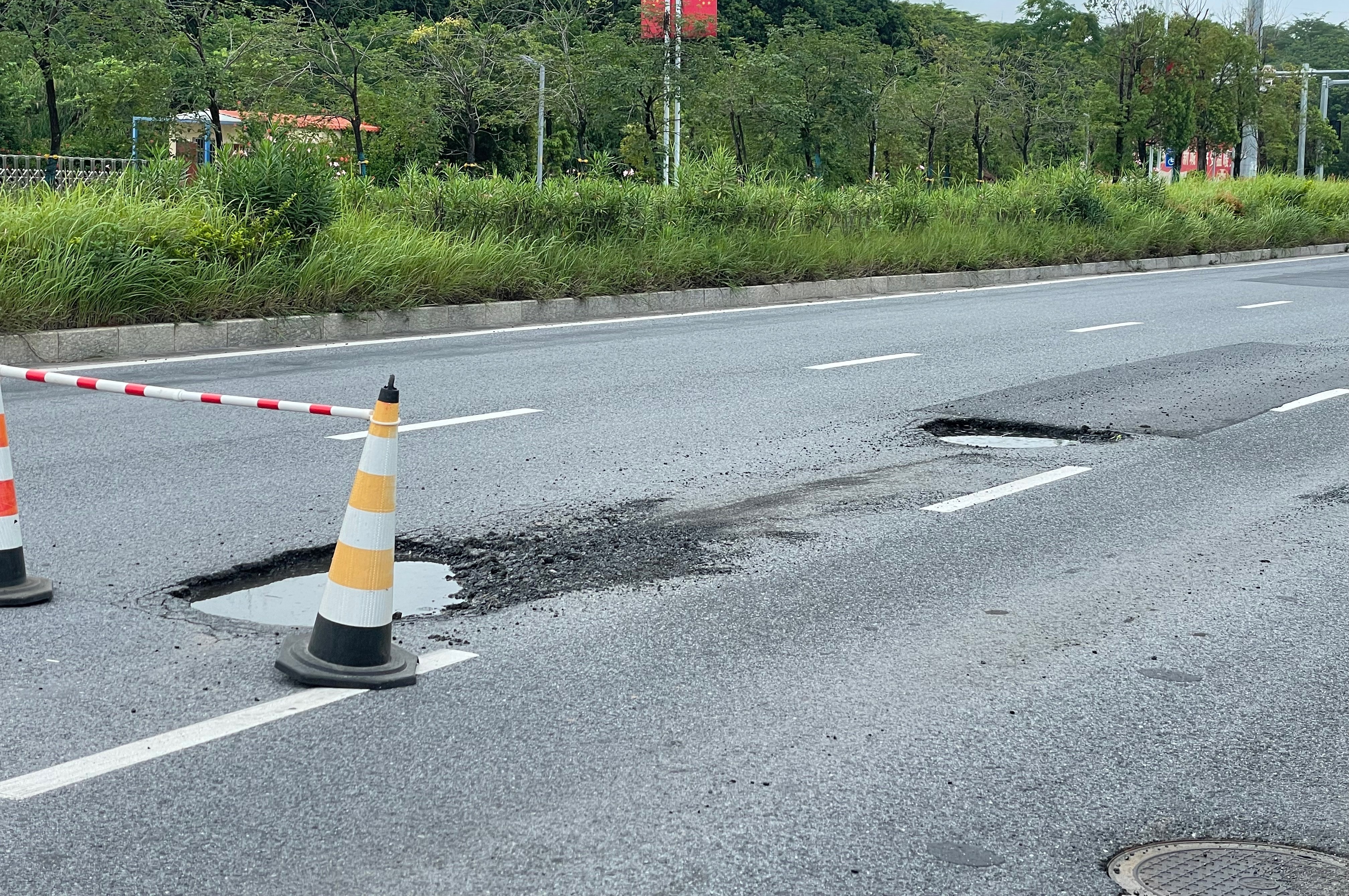 【玉林某道路的机动车道上有两个路坑】6月27日，网友爆料称：玉林市某道路红绿灯路