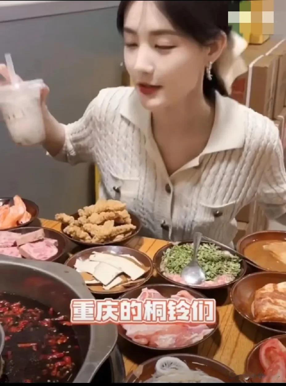 李一桐吃火锅，穿着浅色针织衫淡妆出镜，面前红油锅底翻滚着辣椒，桌上摆满毛肚、黄喉
